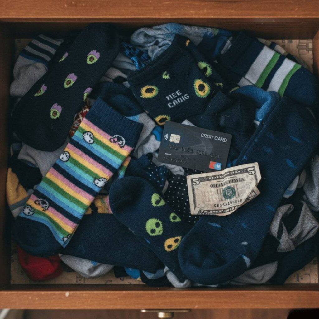 An overhead shot of a sock drawer filled with mismatched socks, a debit card, and a crumpled $5 bill.