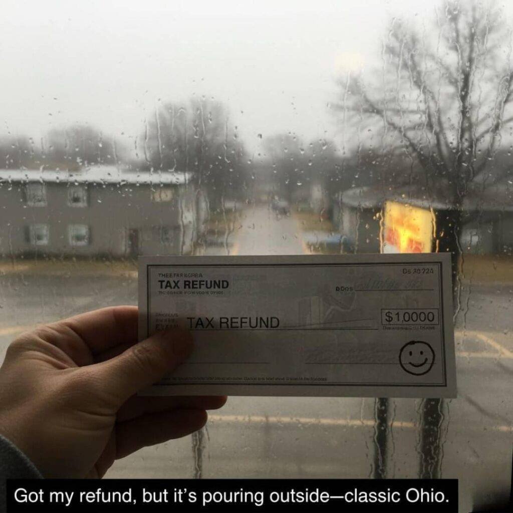 A hand holding a tax refund check with a smiley face doodled on it, outside a rainy window.